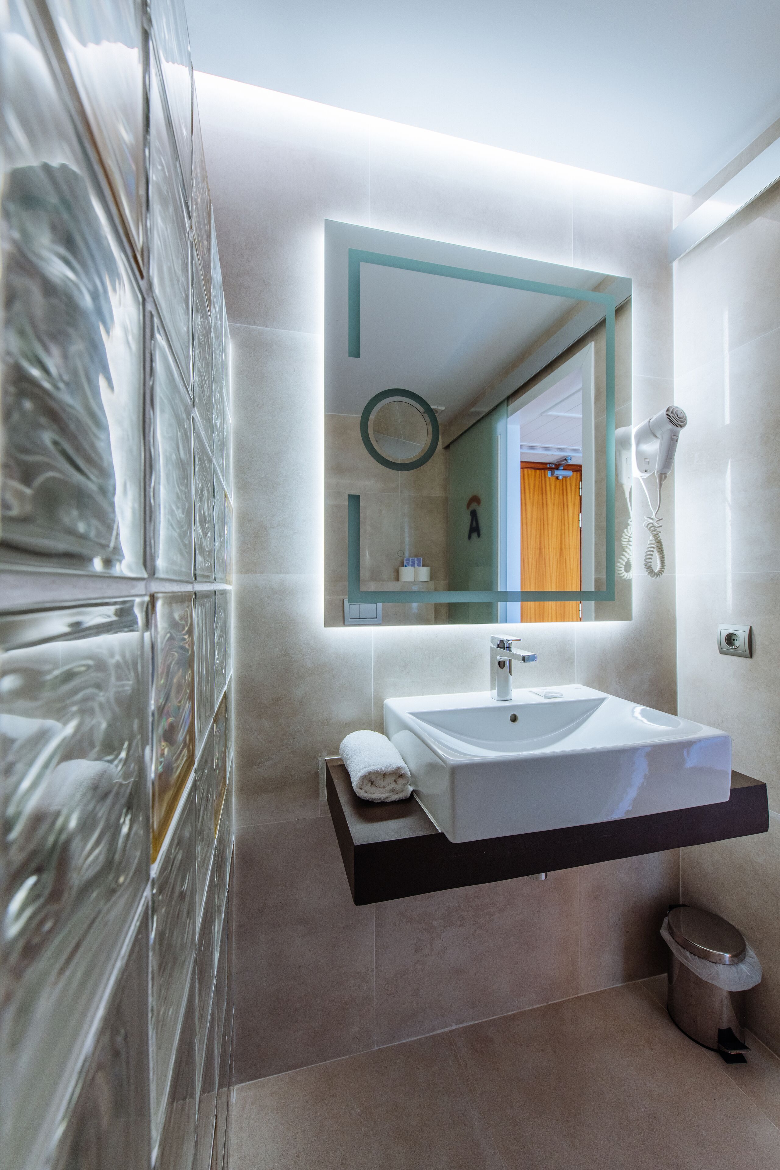 Une salle de bain moderne avec un grand miroir, un lavabo blanc et une serviette posée sur le comptoir.
