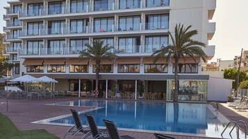 A multi-story hotel with a pool area, outdoor seating, and palm trees.
