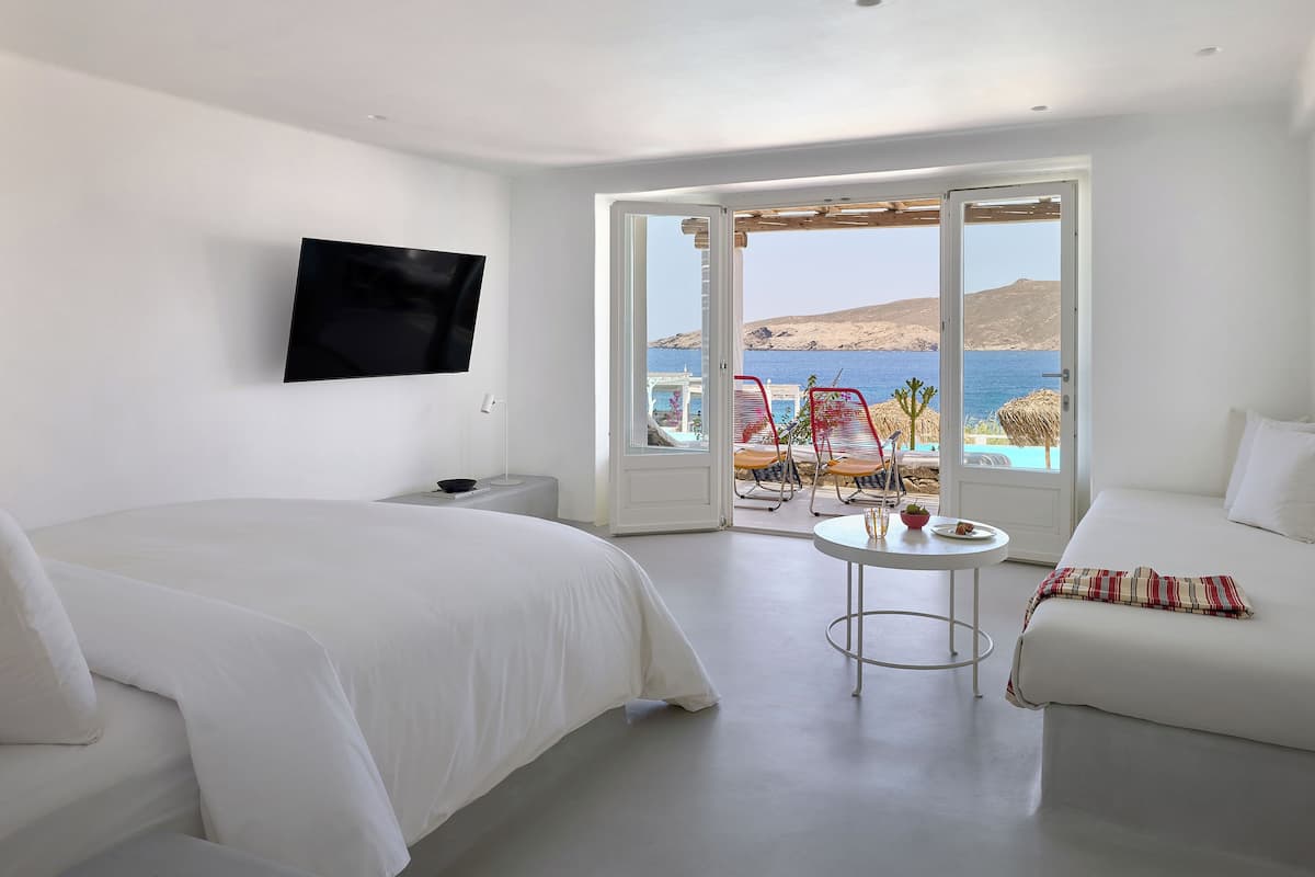 A hotel room with a bed, a TV, a small table, and a view of the sea.