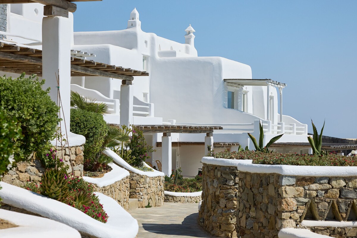 A white building with a stone pathway leading to it, surrounded by greenery and a clear blue sky.
