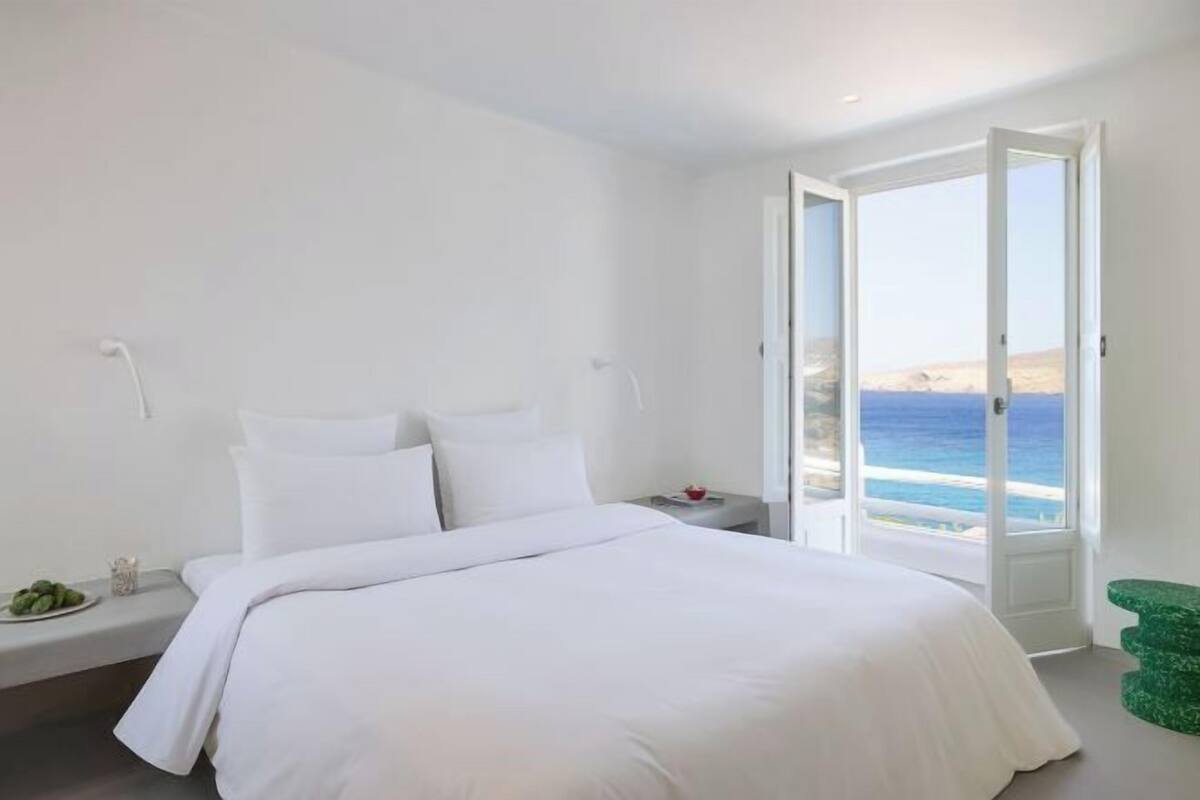 A bedroom with a bed, a nightstand, a green chair, and a view of the ocean.
