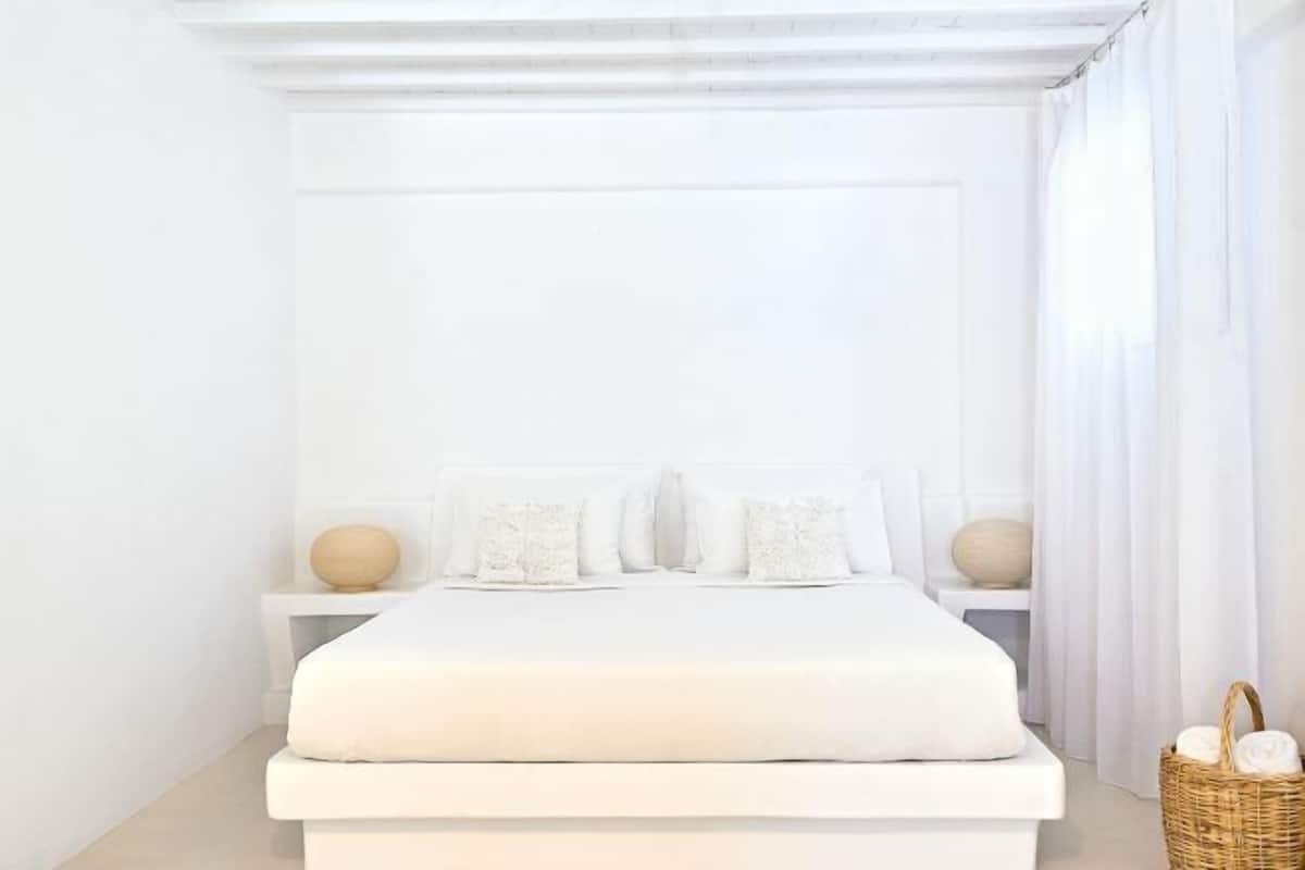 A minimalist white bedroom with a large bed, two bedside tables, and a wicker basket.