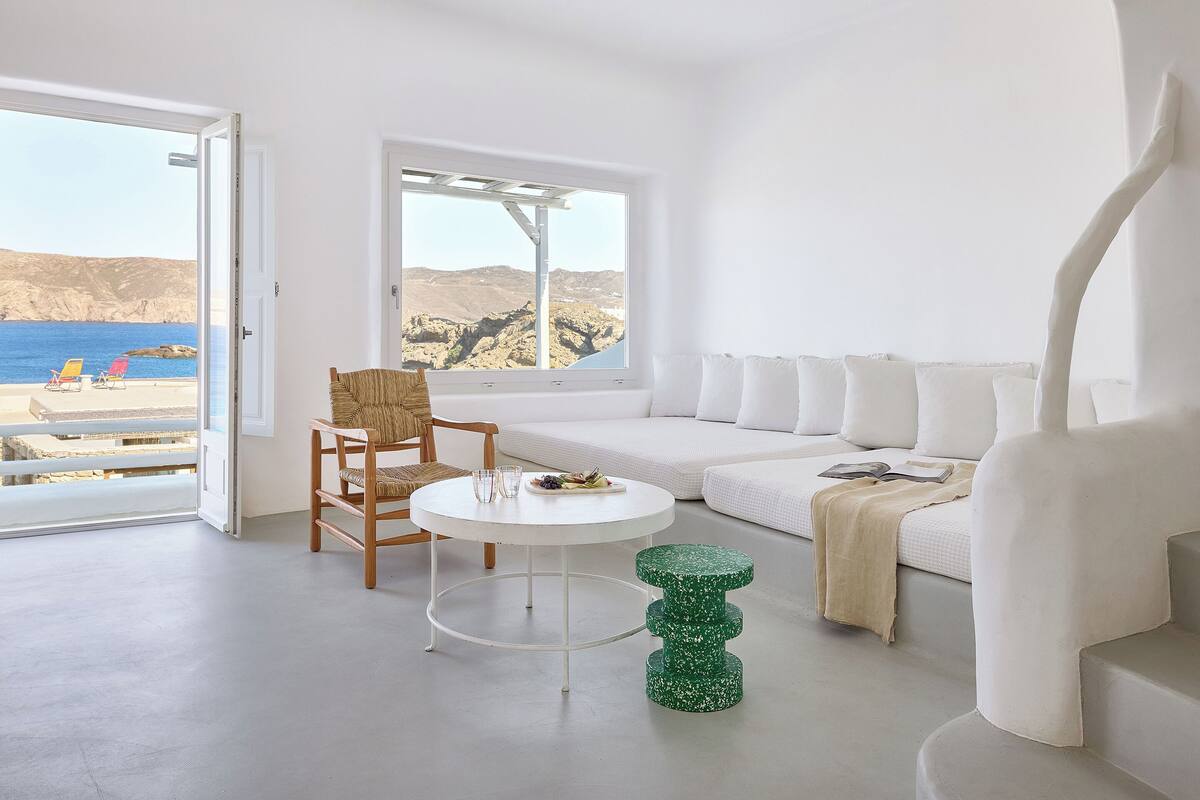 A minimalist room with a white sofa, a wooden chair, a small round table, and a green accent piece.