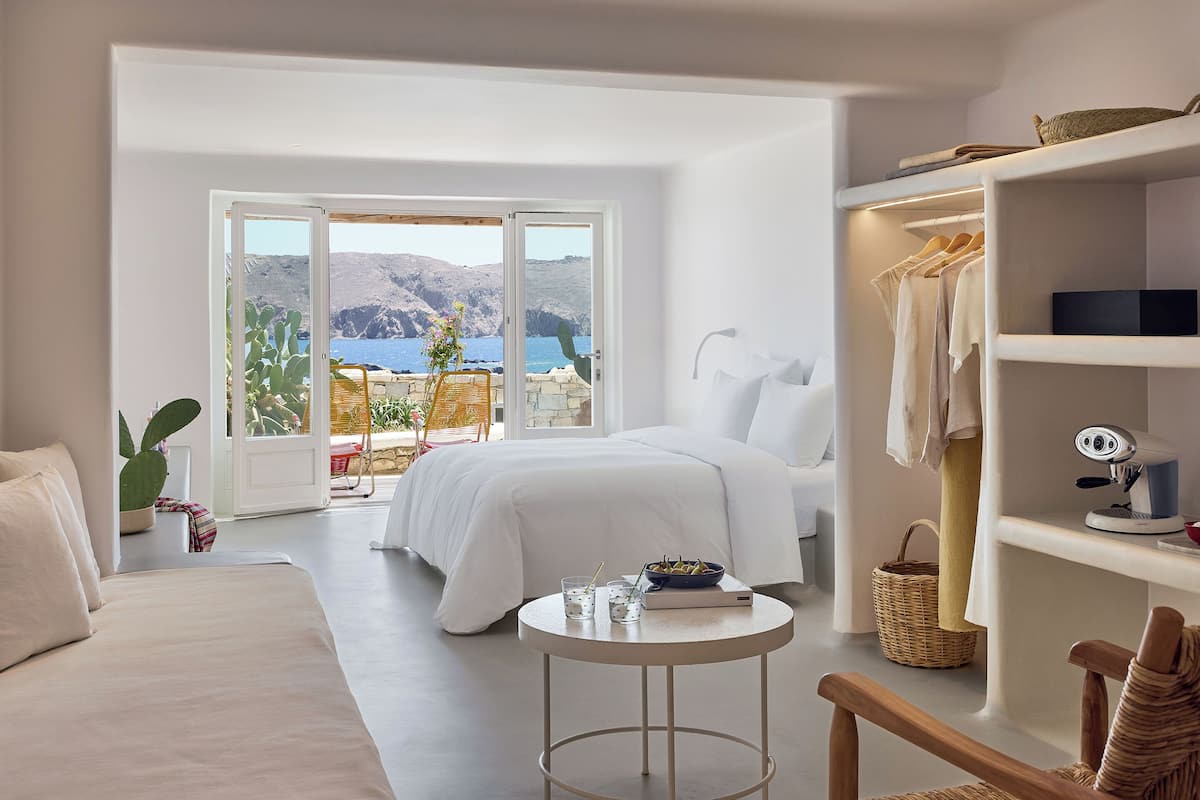A bedroom with a bed, a small round table, a wardrobe, and a view of the sea.