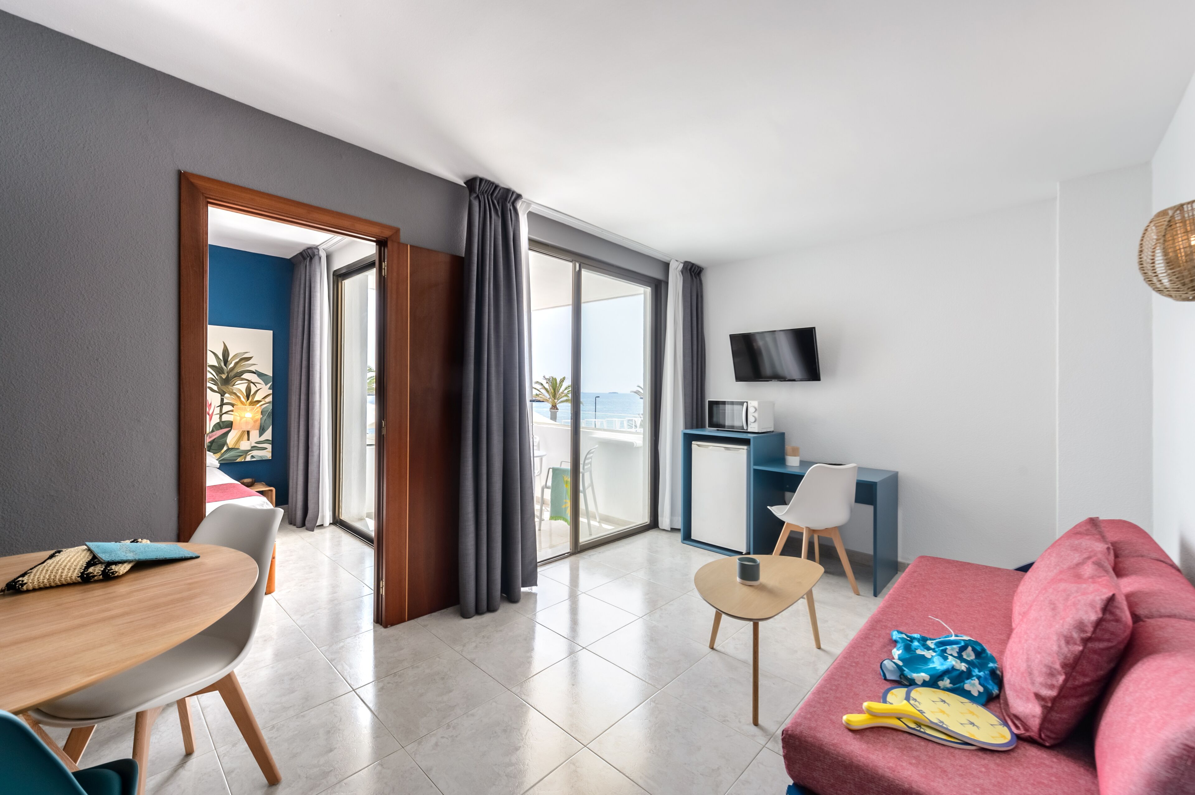 Habitación de hotel moderna con comedor, sofá, televisión y balcón con vistas.