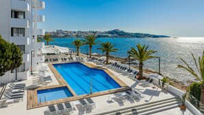 A rooftop pool with clear blue water, surrounded by lounge chairs and palm trees, overlooking a coastal cityscape. - Apartamentos Vibra Jabeque Soul (Ibiza Town)