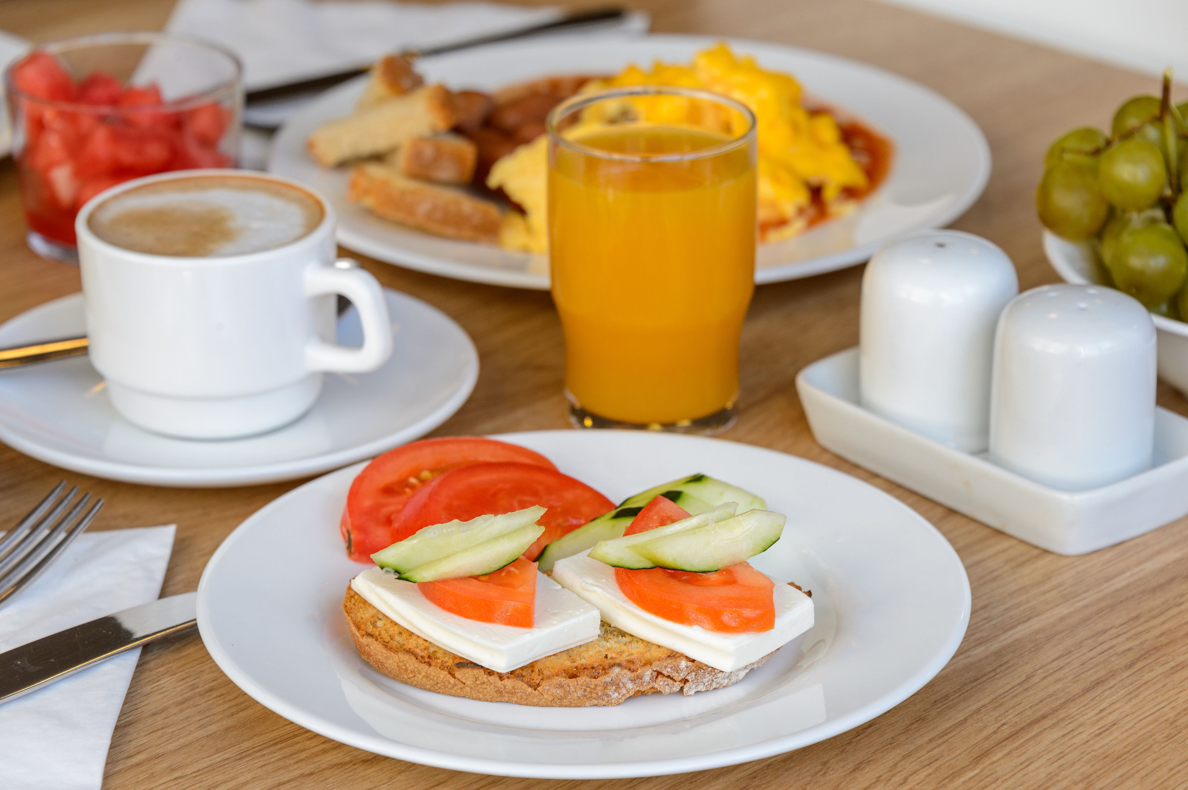 A breakfast setting with a plate of toast topped with tomatoes and cucumbers, a glass of orange juice, and a cup of coffee.
