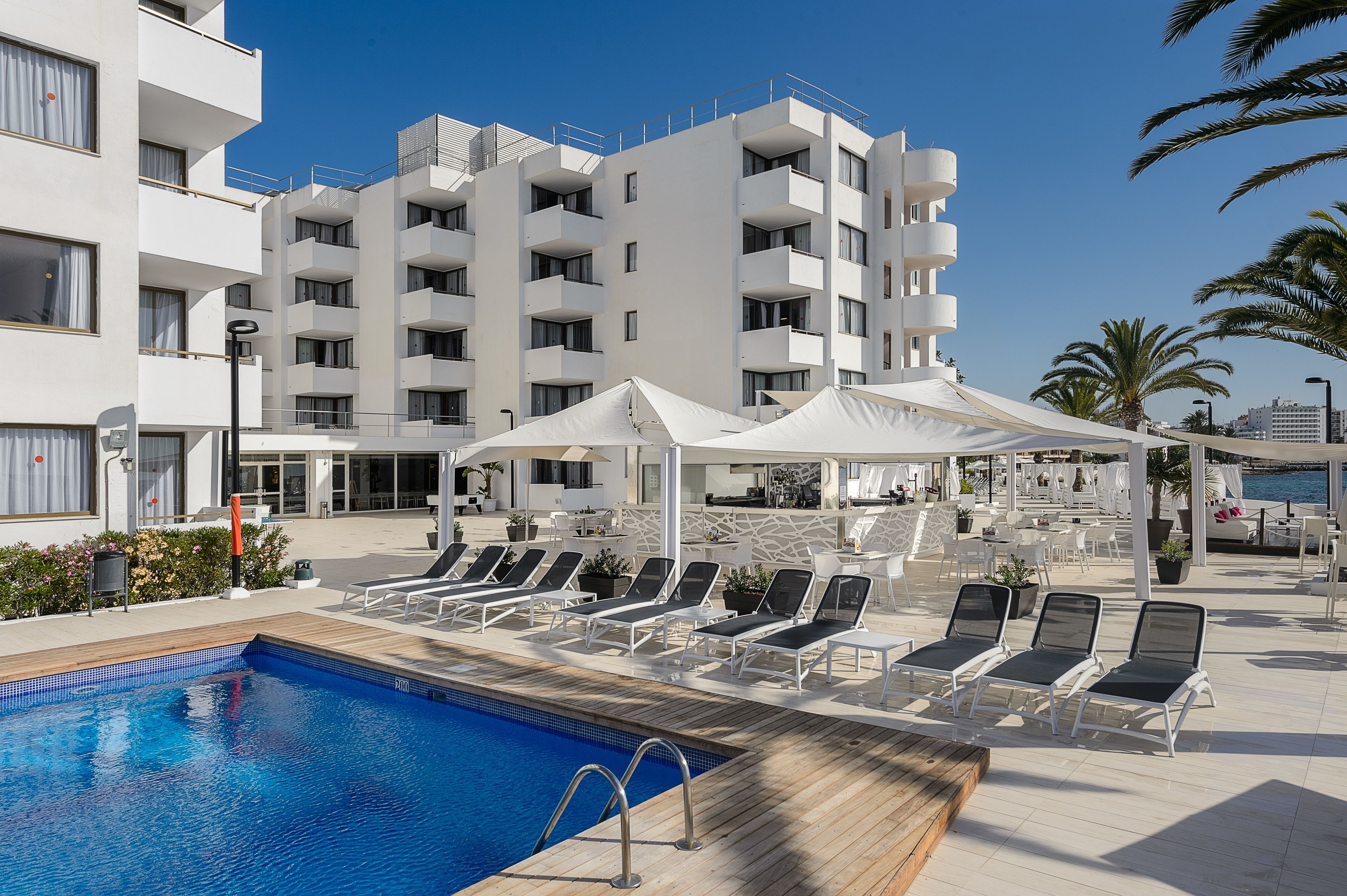 Un hôtel moderne doté d’une piscine, de chaises longues et d’un espace salon couvert.
