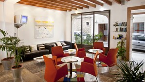 A modern interior with a sofa, orange chairs, a coffee table, and potted plants. - L'Hostal hotel d'interior (Pollenca)