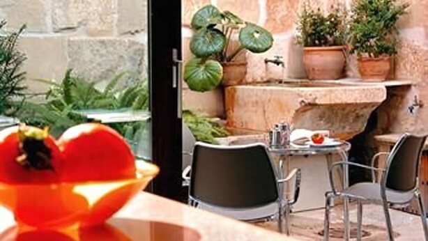 An outdoor dining area with stone walls, potted plants, and a table with chairs. - L'Hostal hotel d'interior (Pollenca)