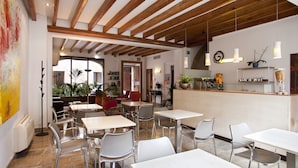 A restaurant with a wooden ceiling, white tables, and chairs. There are plants and a counter with a shelf. - L'Hostal hotel d'interior (Pollenca)