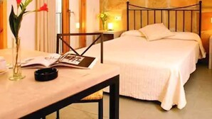 A hotel room with a bed, bedside table, lamp, and a vase with flowers. - L'Hostal hotel d'interior (Pollenca)