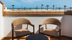 A balcony with two wicker chairs and a small table, overlooking a beach with palm trees and the ocean. - Hotel Tarik (Torremolinos)