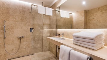 A modern bathroom with a glass-enclosed shower, a sink with a mirror, and neatly stacked towels.