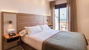 A hotel room with a large bed, a bedside table with a phone, and a view of the beach through a large window. - Hotel Tarik (Torremolinos)