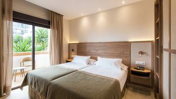 A hotel room with two beds, a balcony, and a view of greenery.