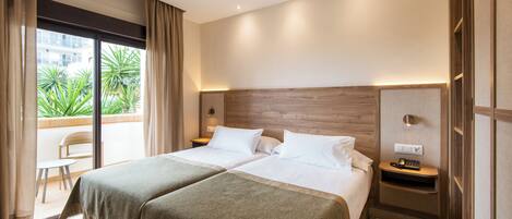 A hotel room with two beds, a balcony, and a view of greenery.