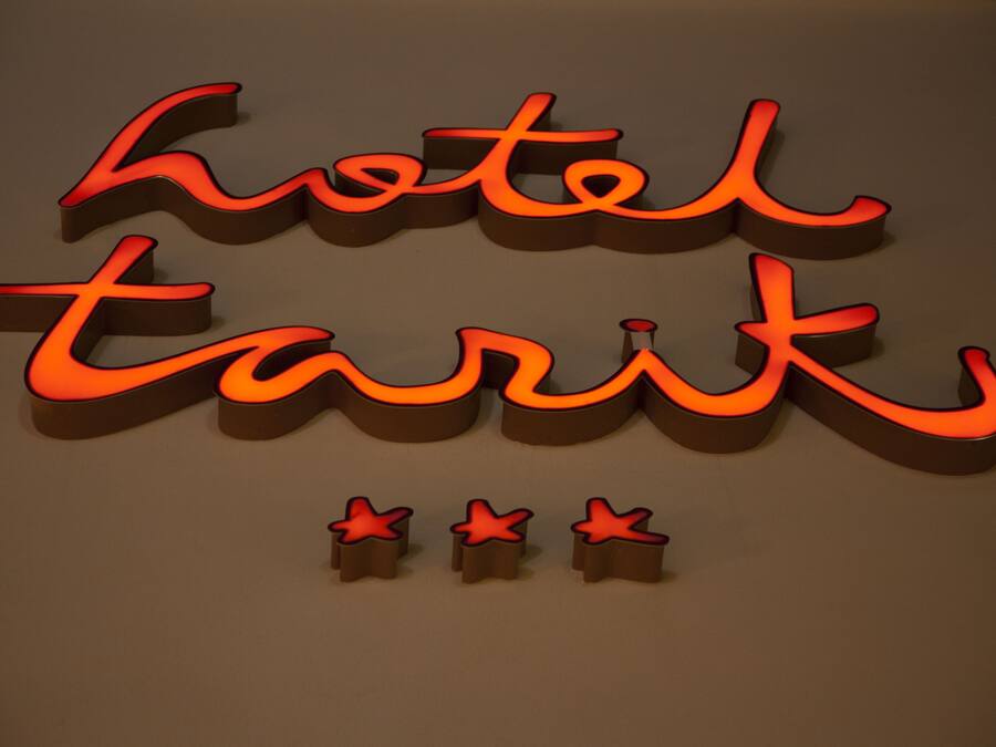 Een verlicht 3D-bord met de woorden 'hotel' en 'tarik' in een gestileerd lettertype, met daaronder drie rode sterren.