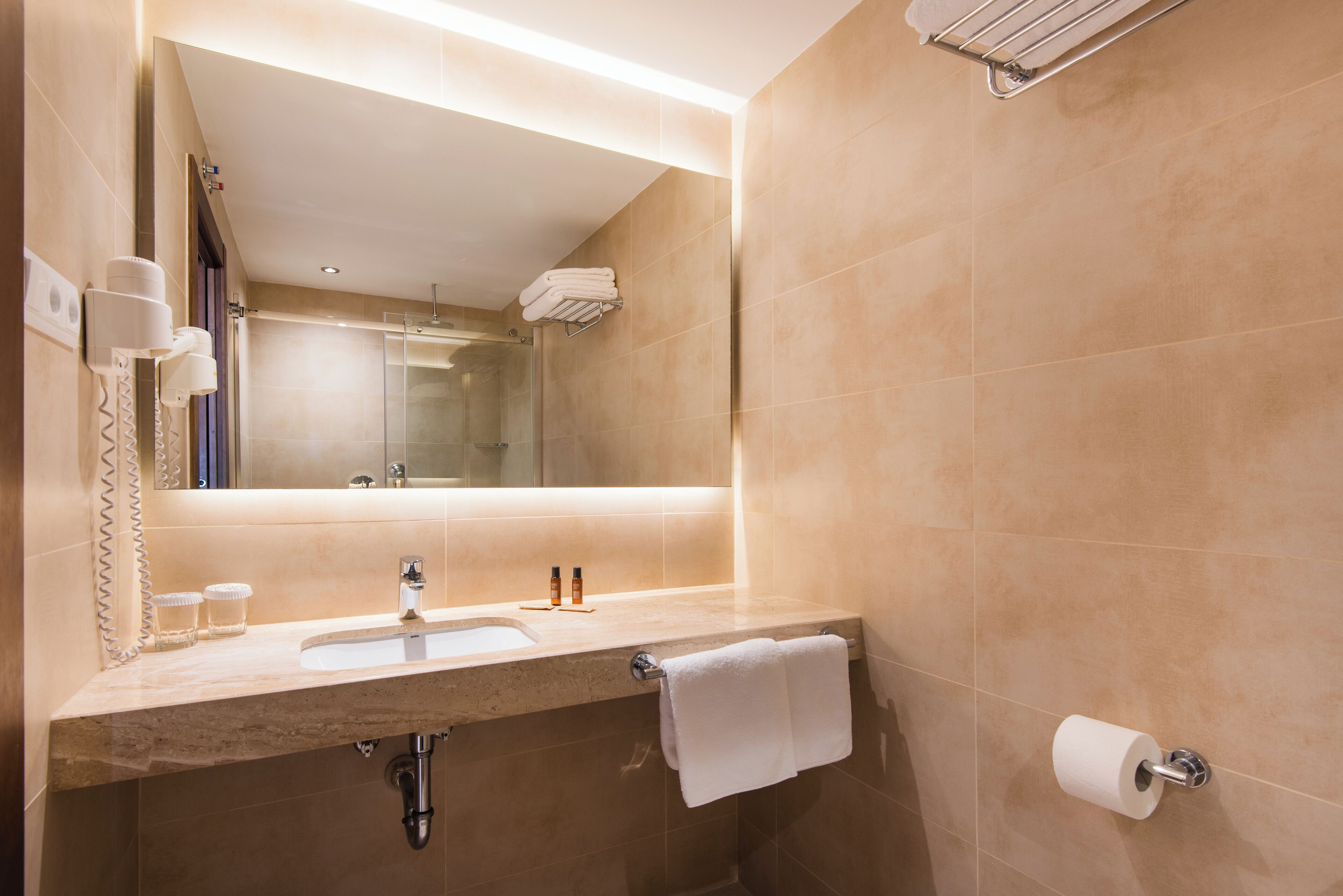 A modern bathroom with a sink, mirror, towel rack, and toilet paper holder.