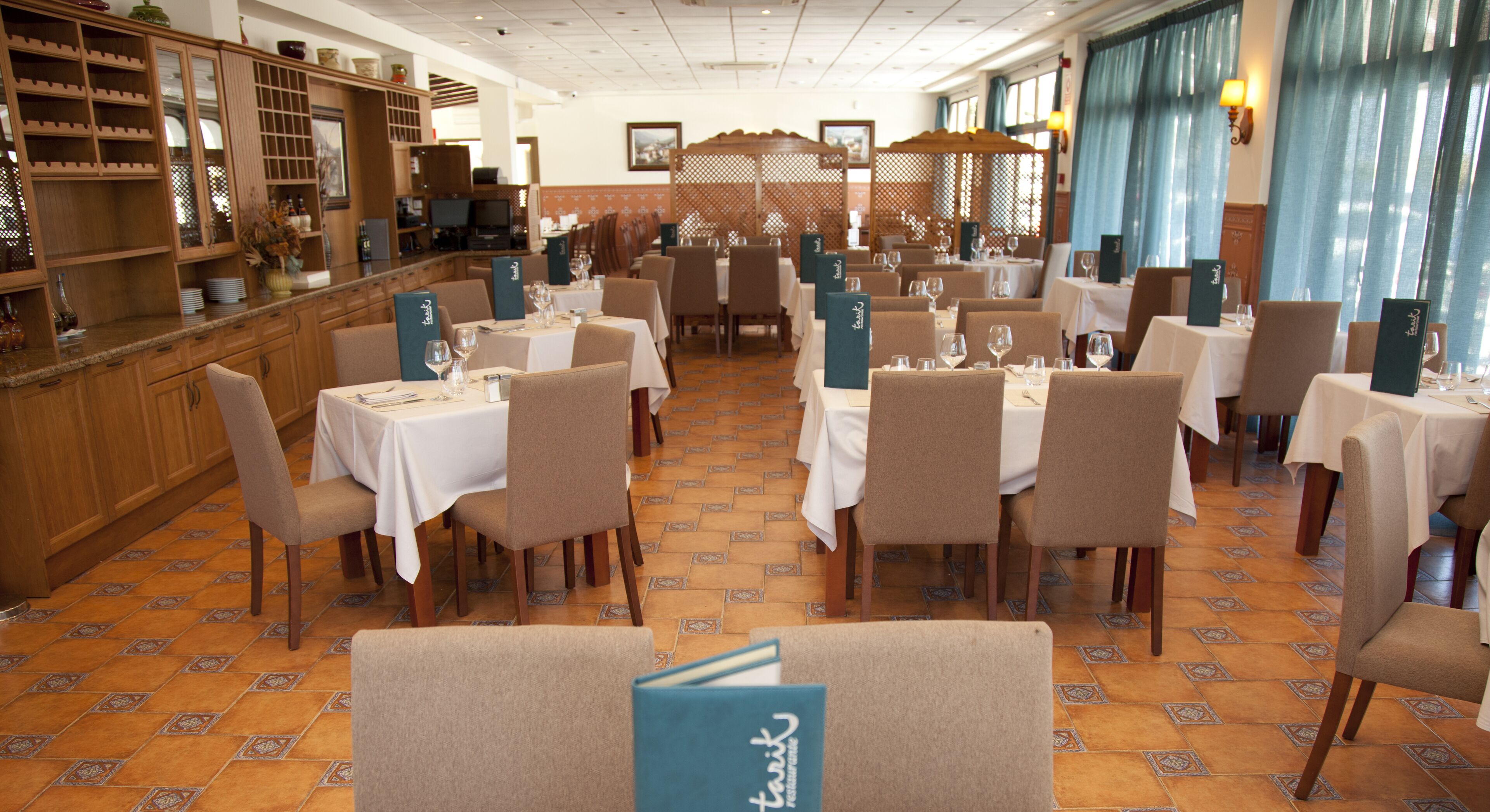 Un restaurante con varias mesas y sillas, una zona de bar y suelo de baldosas.