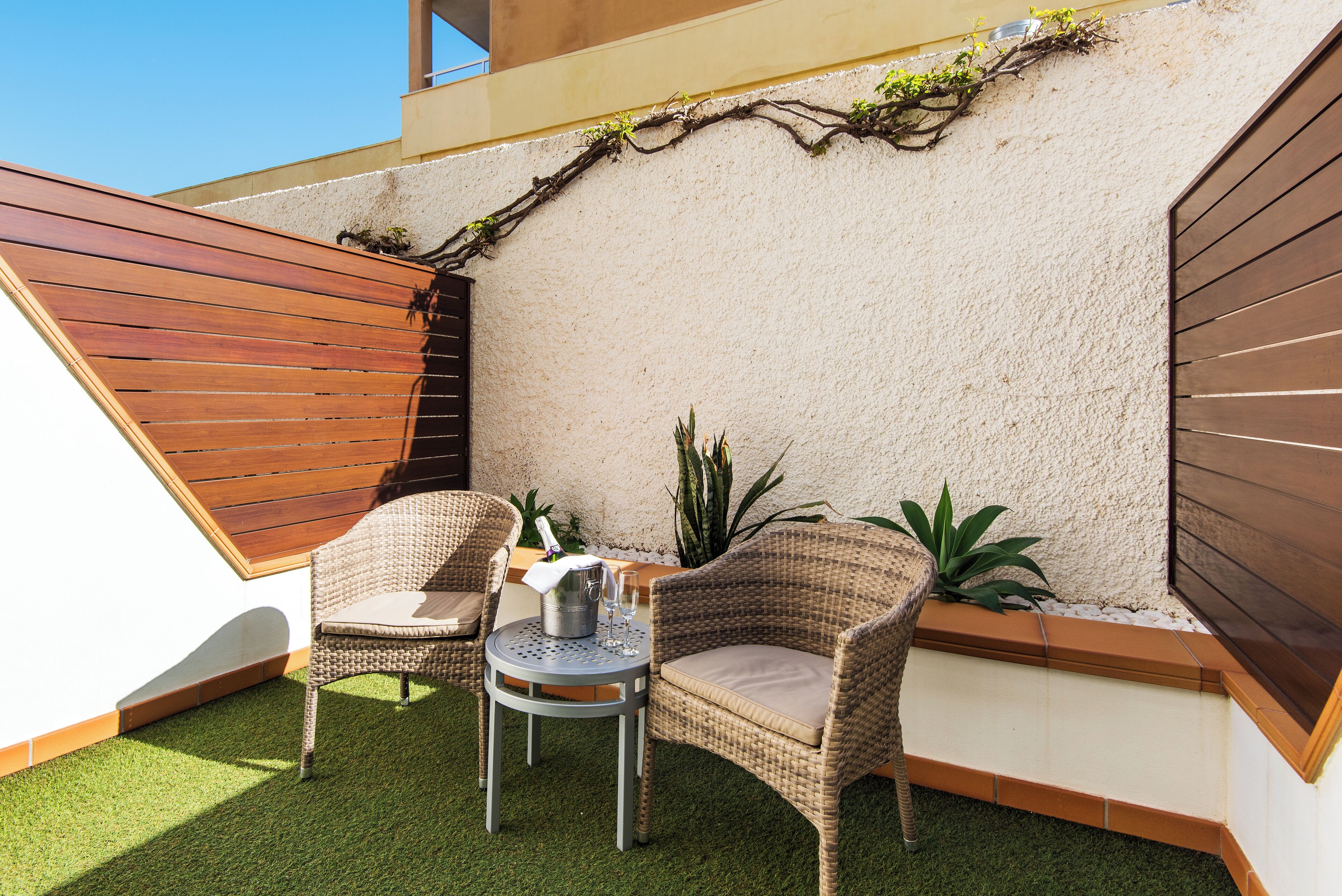 Un petit espace patio avec deux chaises en osier, une petite table ronde et une plante en pot.