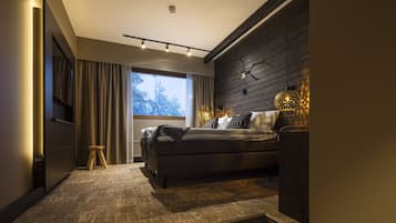 Un dormitorio moderno con una cama grande, un taburete pequeño, un televisor y una ventana con cortinas.