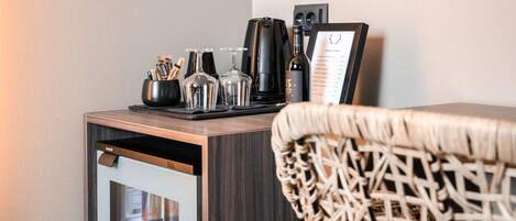 A hotel room with a minibar, a coffee maker, wine glasses, and a menu stand.