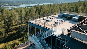 Eine Dachterrasse mit Sitzgelegenheiten im Freien, Blick auf einen See und eine bewaldete Landschaft.