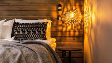 A cozy bedroom with a wooden headboard, a patterned pillow, a throw blanket, and a hanging light fixture.