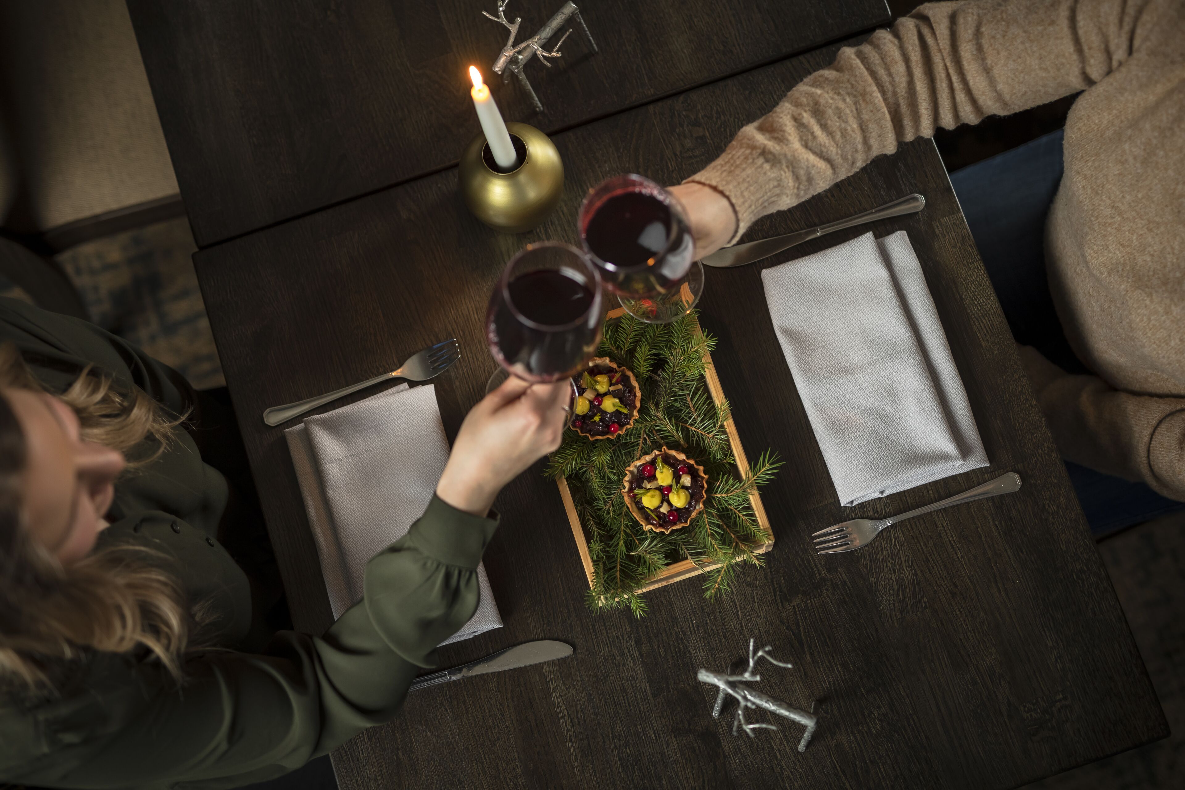Una mesa con dos copas de vino tinto, una vela y una bandeja con pastelería.