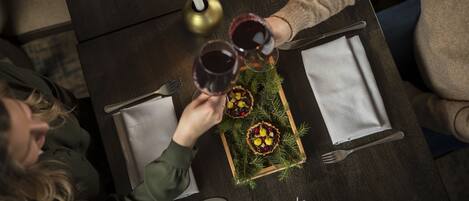 Una mesa con dos copas de vino tinto, una vela y una bandeja con pastelería.