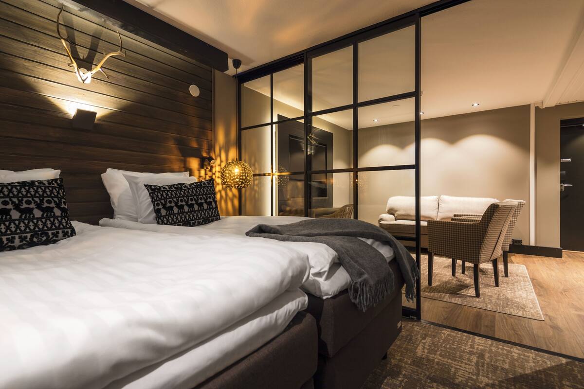 Habitación de hotel moderna con una cama grande, un espacio de descanso con una silla y vistas a través de un panel de vidrio.