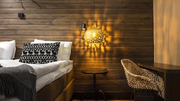 Un dormitorio moderno con un panel de madera en la pared, una cama con almohadas estampadas, un sillón tejido y una mesa con una lámpara original.