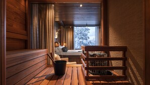 L’intérieur chaleureux d’un chalet en bois, avec un coin salon, une table et une vue sur un paysage enneigé par la fenêtre.