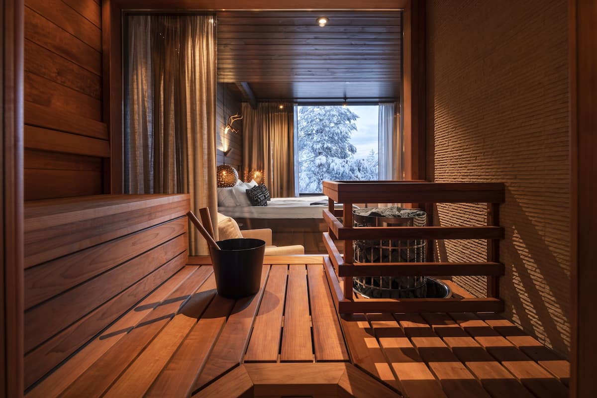 Interior acogedor de una cabaña de madera, con una zona de estar, una mesa y vistas a un paisaje nevado a través de una ventana.