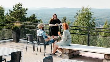 Eine Terrasse mit Sitzgelegenheiten im Freien, Blick auf die Landschaft und eine stehende Person.