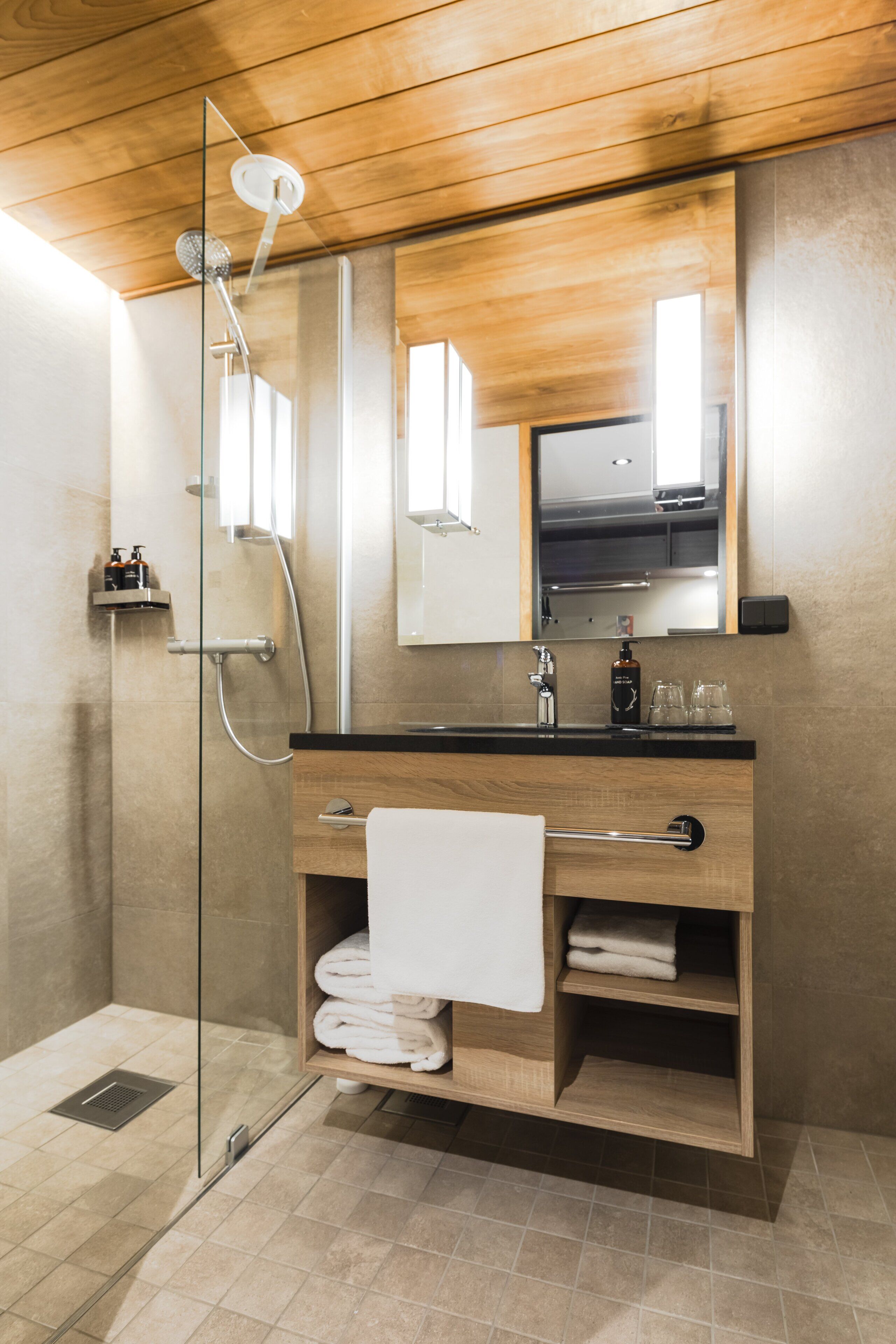 Un baño moderno con cabina de ducha de vidrio, tocador de madera y un espejo grande.