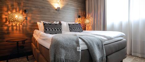 A modern bedroom with a wooden wall, a bed with patterned pillows, a grey blanket, and two wall-mounted lamps.