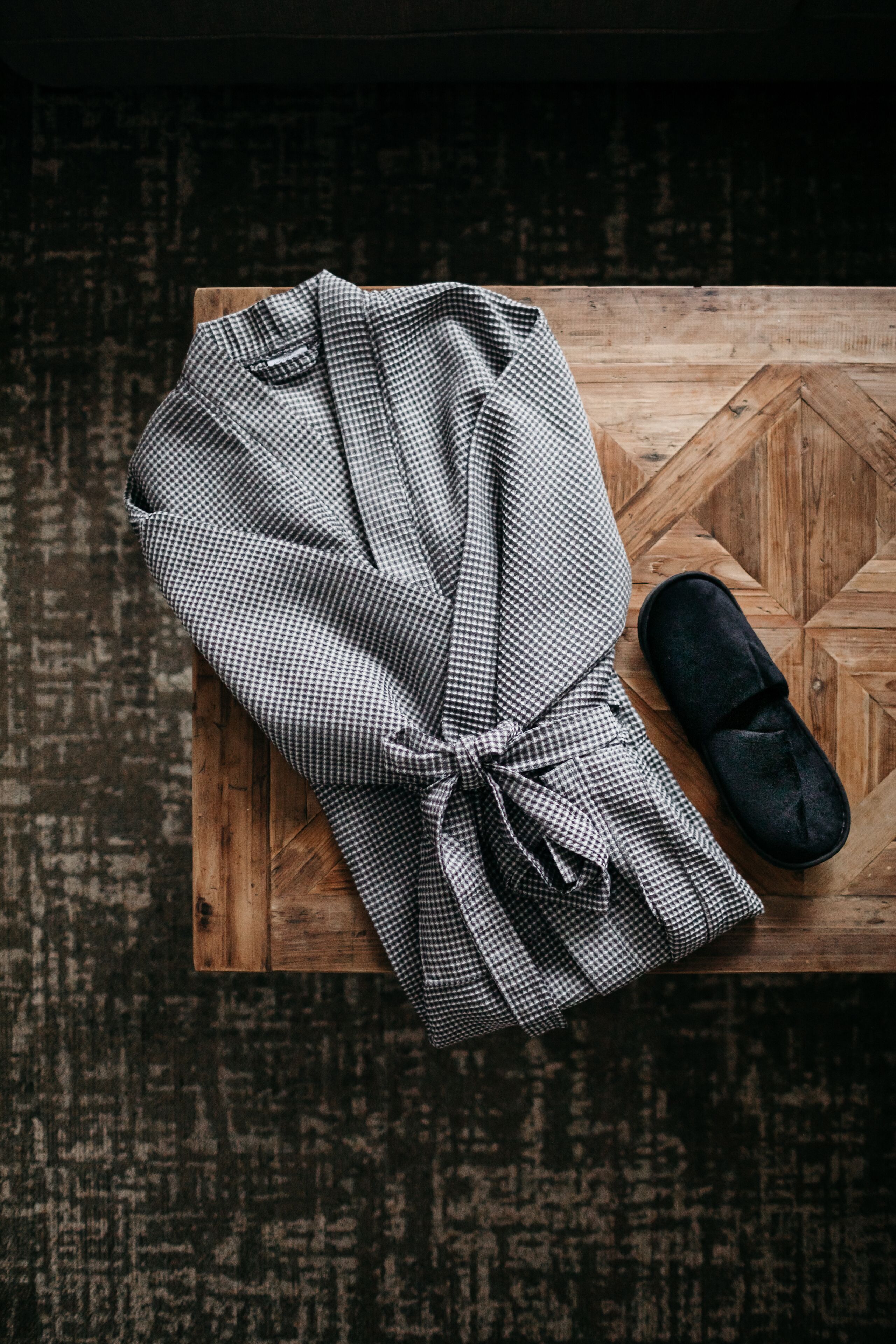 Une robe à carreaux et une pantoufle noire sur une table en bois ornée d’un motif géométrique.