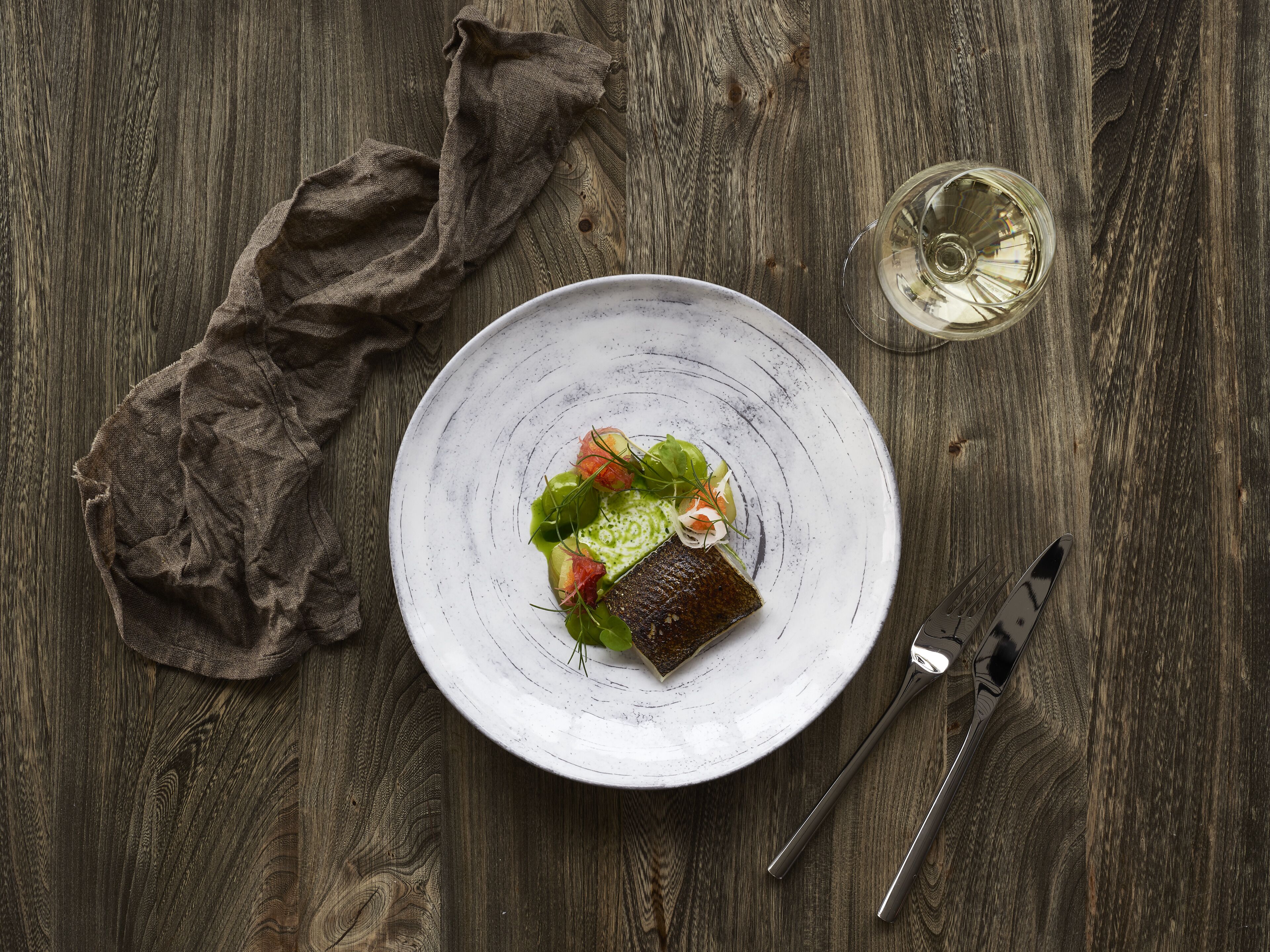A plate of food on a wooden table with a cloth napkin and a wine glass.