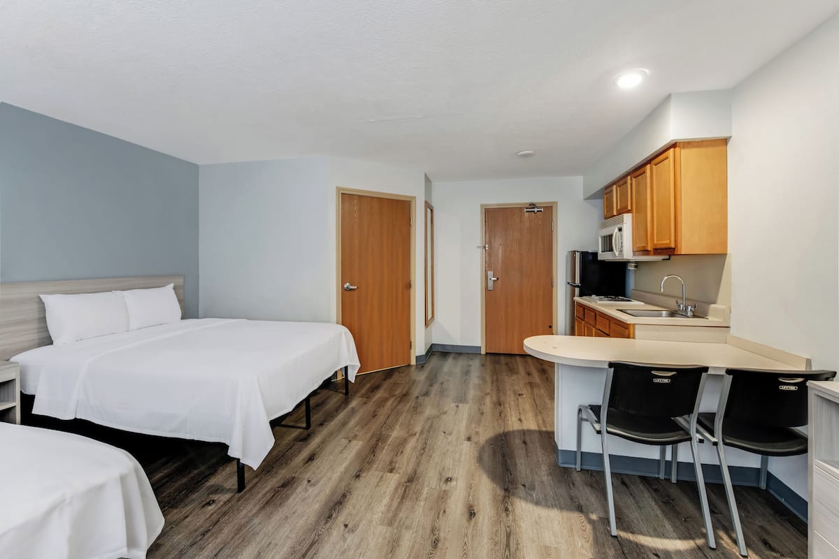 Een kleine hotelkamer met twee éénpersoonsbedden, een kitchenette en een klein barretje.