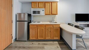 A compact kitchen with wooden cabinets, a stainless steel refrigerator, a microwave, a sink, and a flat-screen TV.