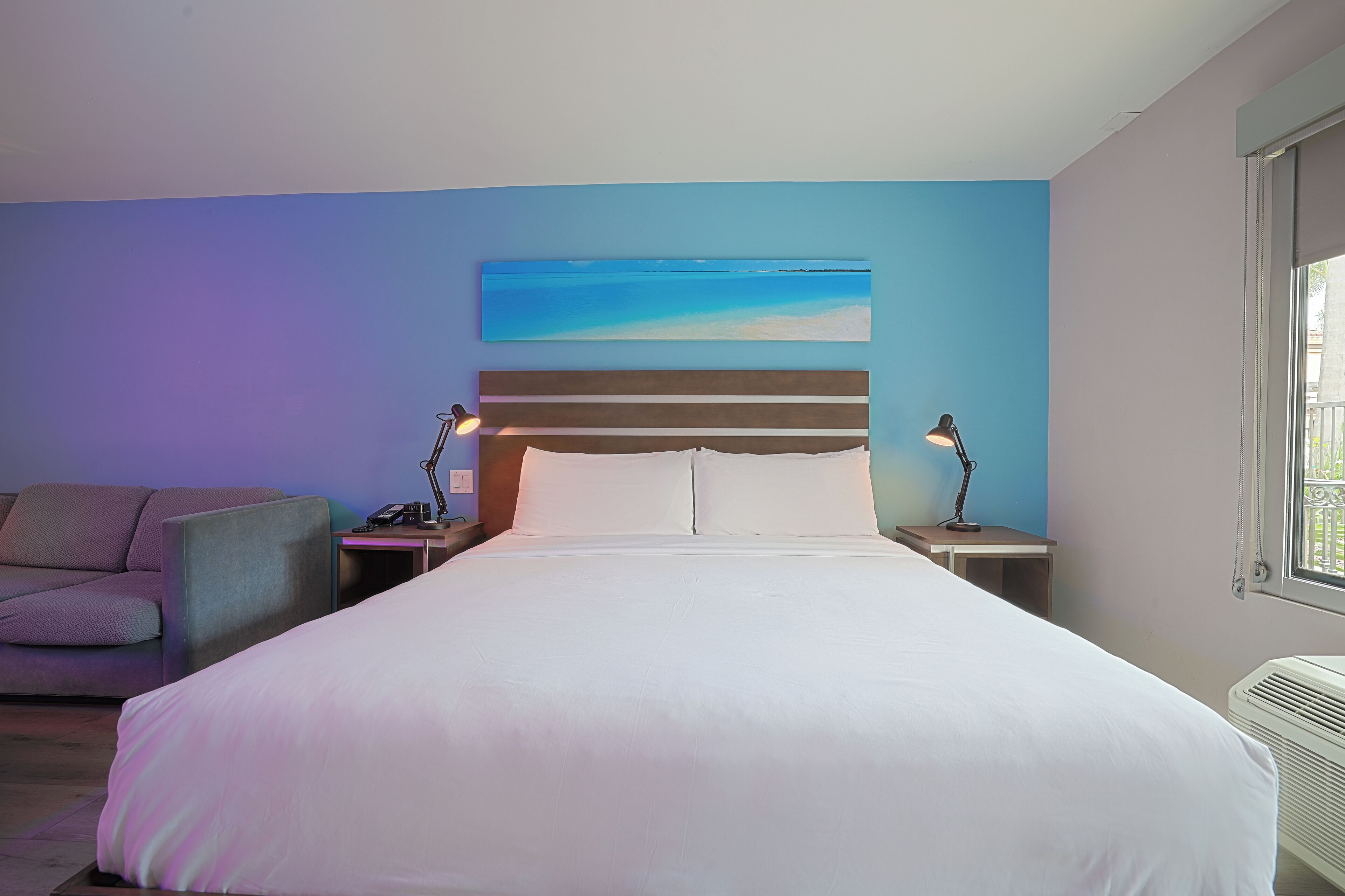 Een slaapkamer met een bed, nachtkastje, lamp, bank en een schilderij aan de muur.