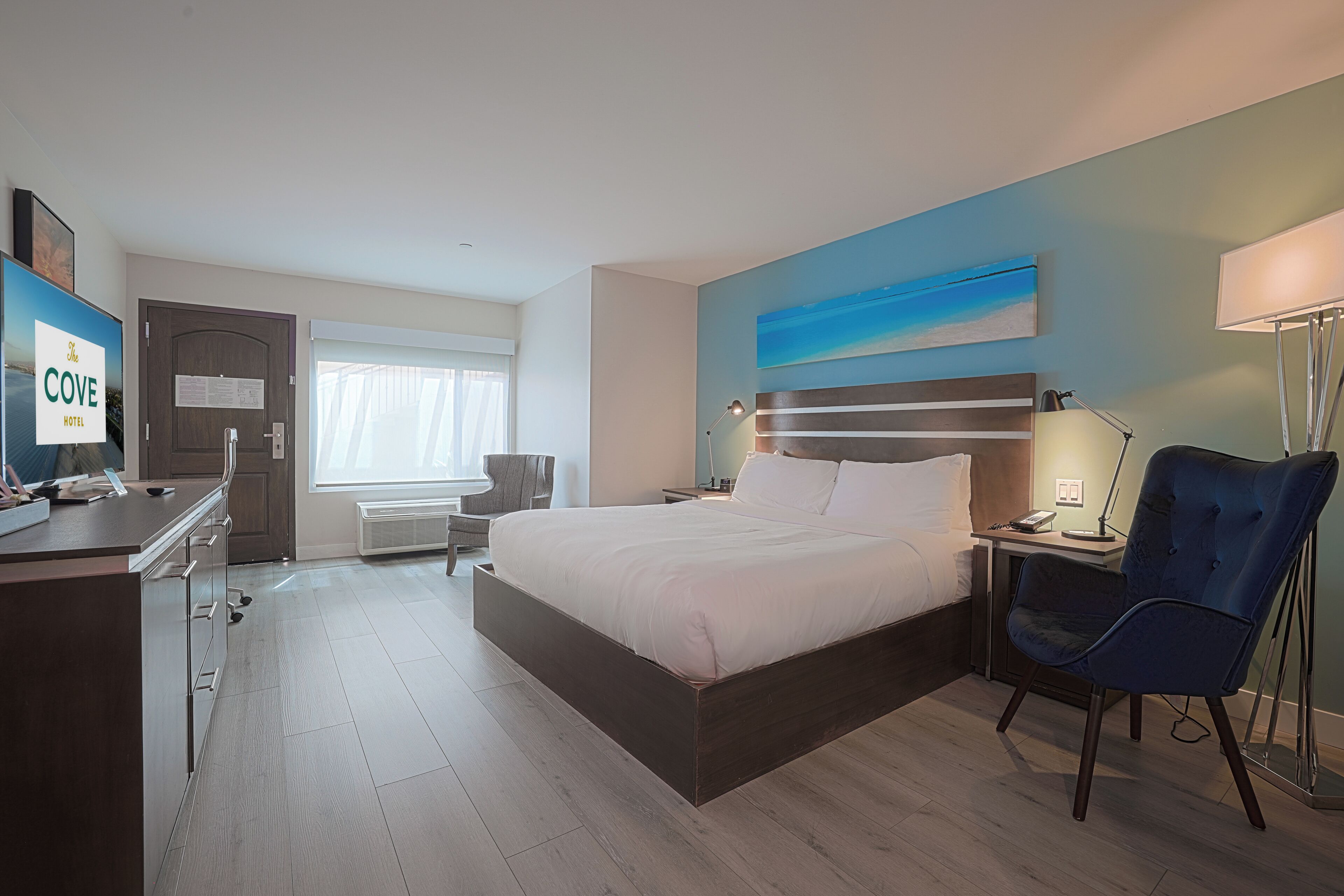 Una habitación de hotel con cama, escritorio, silla y un cuadro en la pared.