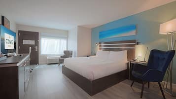 Quarto de hotel com cama, escrivaninha, cadeira e um quadro na parede.