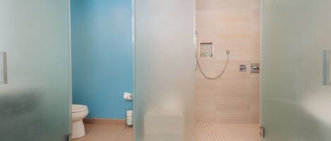 A bathroom with a glass-enclosed shower, a toilet, and a sink with a towel dispenser.