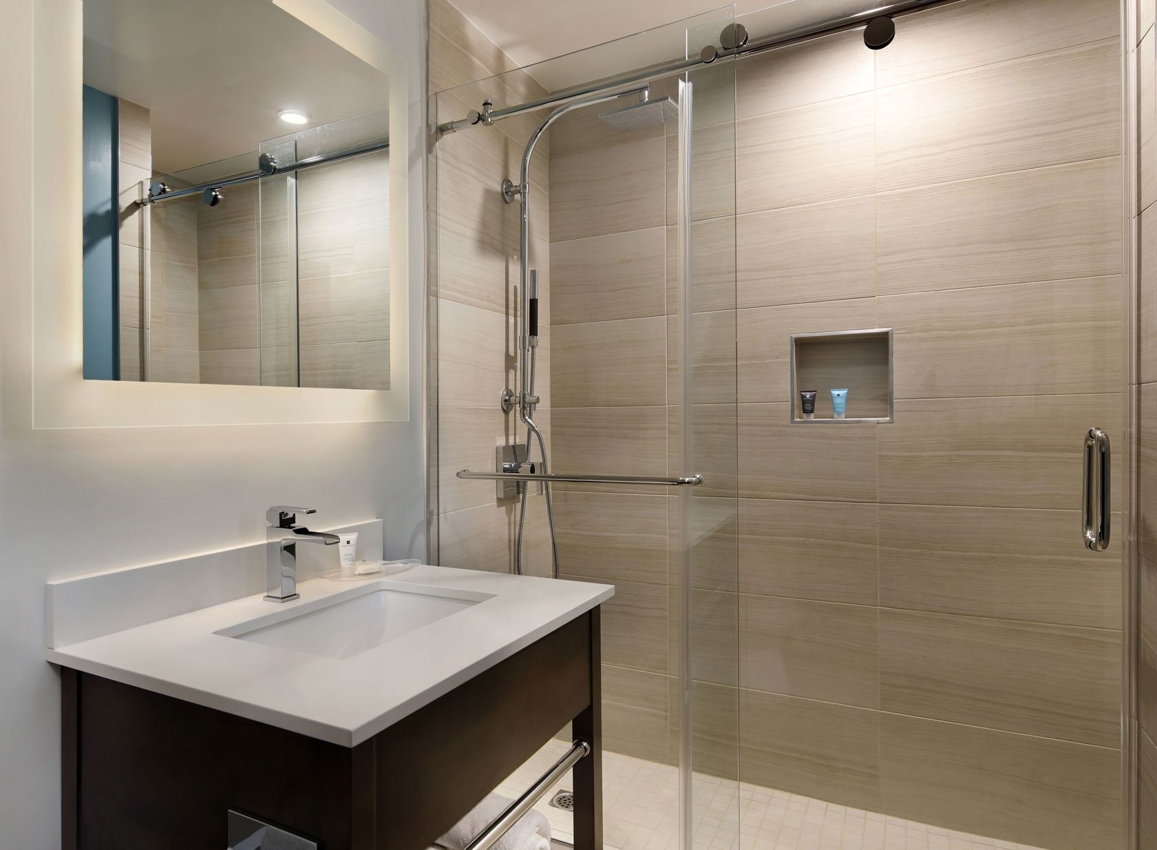 A modern bathroom with a glass shower enclosure, a white sink, and a mirror.
