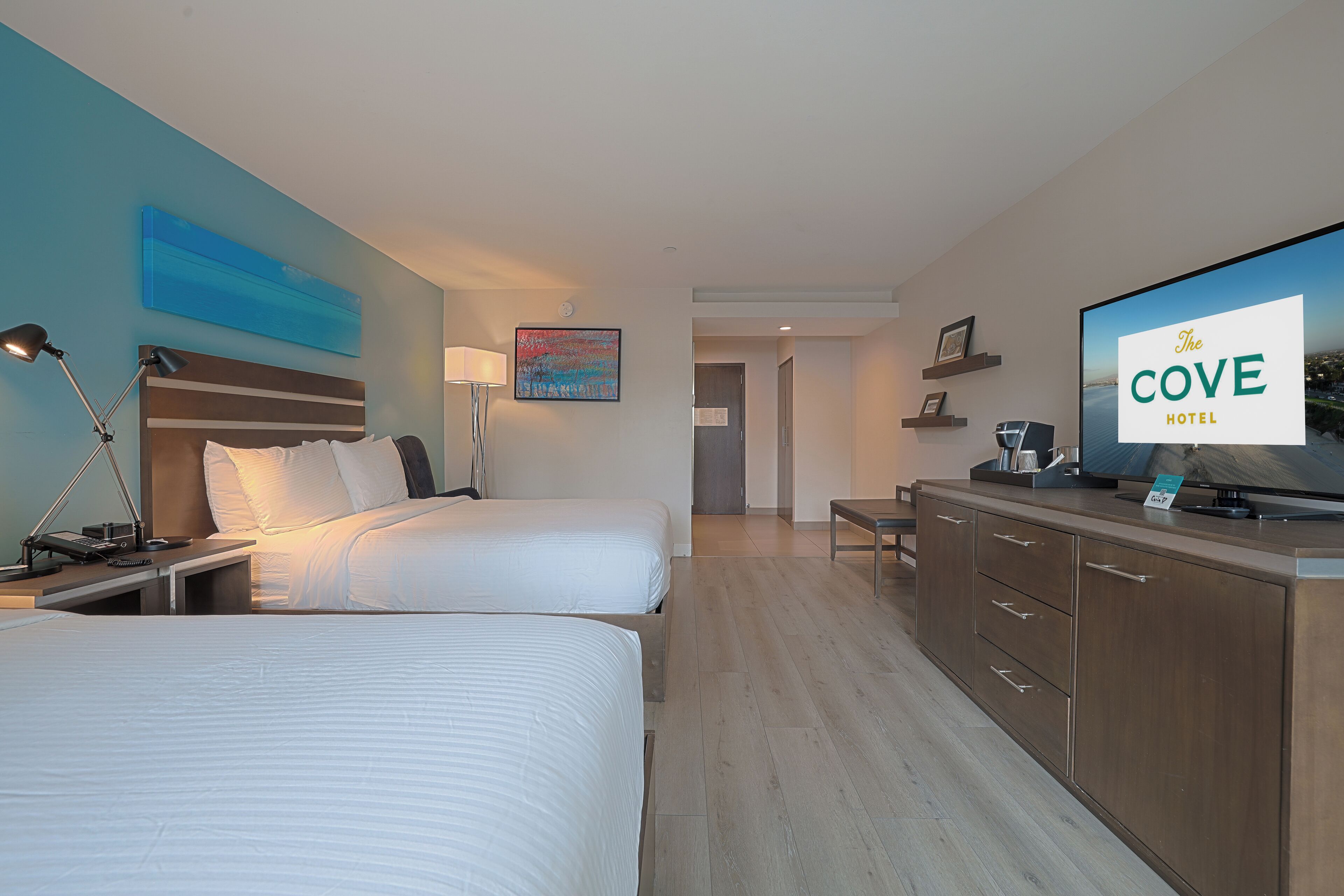 Habitación de hotel con dos camas, un escritorio, televisión y baño a la vista.