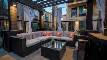 Un área de estar exterior con un sofá modular, una mesa de centro de vidrio y una estructura de pérgola.
