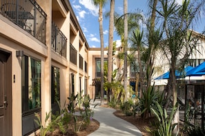 Stroll through a serene corridor lined with lush tropical plants and palm trees, featuring balconies with metal railings.